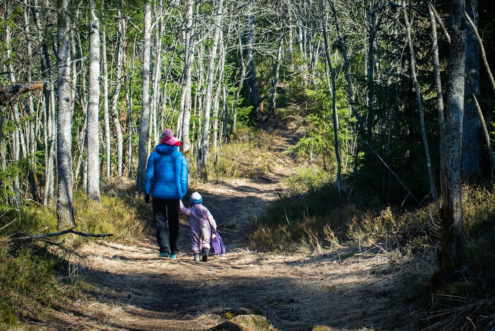 woman in red jacket and blue denim jeans walking on dirt road in forest during daytime