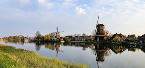 Molens langs een rustige rivier, lage huizen in de verte