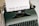 A vintage typewriter with a sheet of paper inserted, displaying the text 'Terms of Service'. The typewriter has a dark green body and black keys, with a brand name on the top right side.