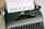 A vintage typewriter with a sheet of paper inserted, displaying the text 'Terms of Service'. The typewriter has a dark green body and black keys, with a brand name on the top right side.