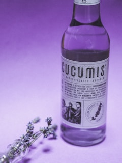 Lilac-toned body splash bottle with a backdrop of blooming lavender and a splash of water.