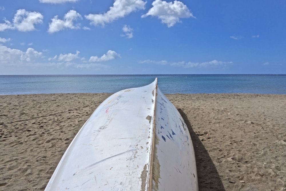 Weißes Surfbrett auf braunem Sand in Meeresnähe unter blauem Himmel tagsüber
