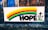 A colorful banner displayed on a metal fence in front of a brick building. The banner features a rainbow with horizontal stripes of yellow, red, green, and blue. Below the rainbow, the word 'HOPE' is written in bold black letters. To the right of the word, there are three black crosses on green bases illustrated.