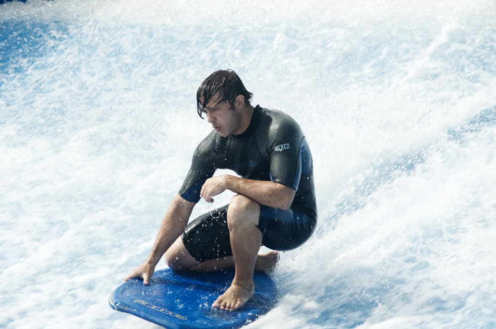 검은 잠수복을 입은 남자가 낮 동안 물 위의 파란색 서핑 보드에 앉아 있습니다.