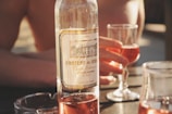 A wine bottle labeled 'Chateau de Jass' is placed on a table. Two glasses filled with rosé wine are visible, one being held by a hand. The setting appears relaxed and sunlit, suggesting a casual outdoor gathering.