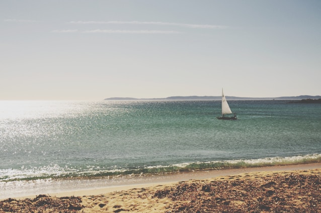 A serene nautical scene featuring a sailboat gliding over calm blue waters under a clear sky.