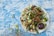 A plate of nachos topped with cheese, olives, lime wedges, cilantro, and avocado slices, placed on a rustic blue and white wooden surface. Next to the plate is a small bowl of black olives and a bowl with more lime wedges.