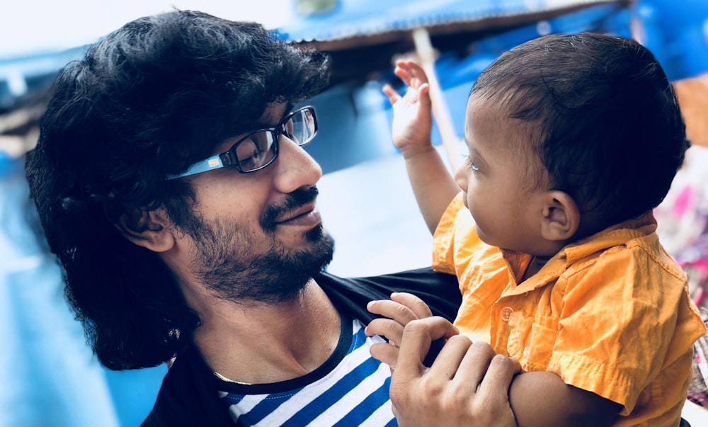 man in black tank top carrying baby in yellow and white stripe shirt