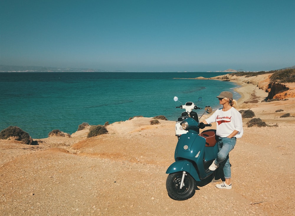 couple sitting on blue motor scooter near sea during daytime