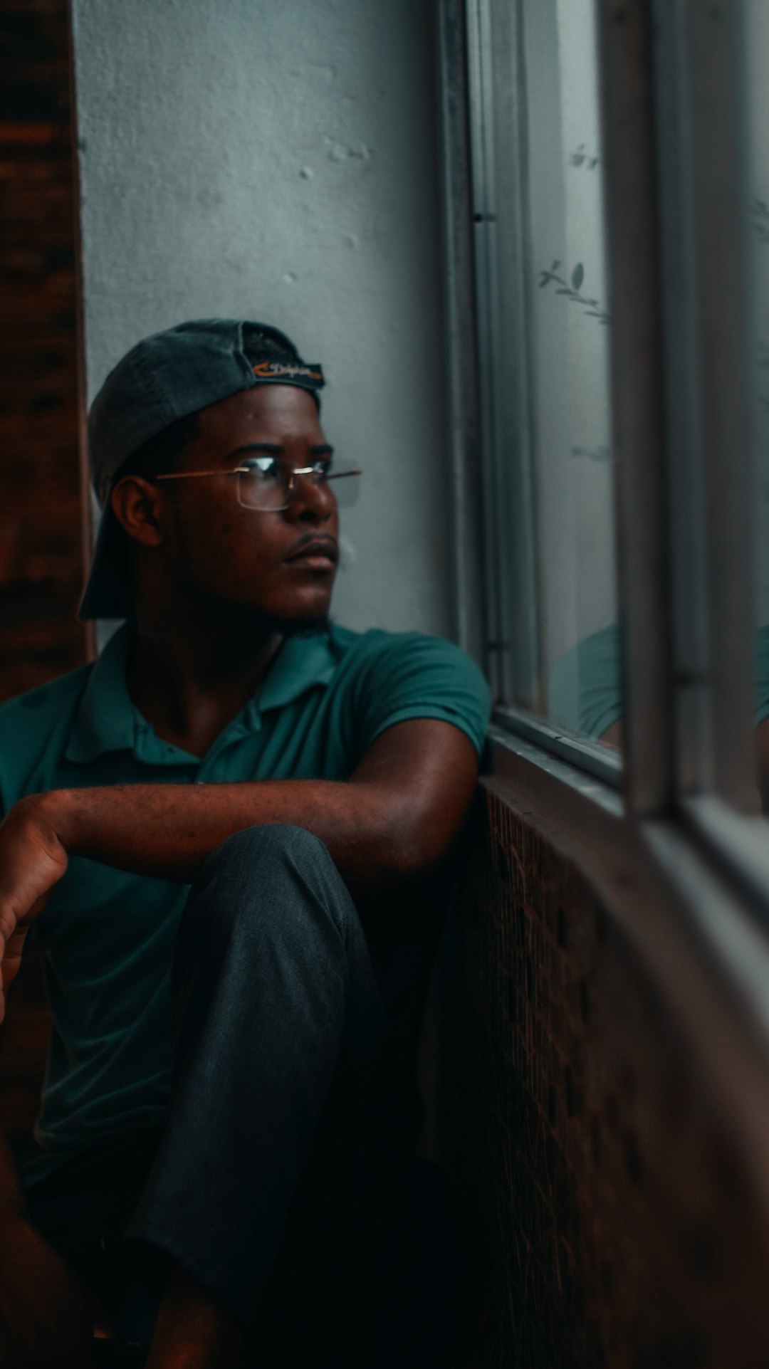 man in blue polo shirt and black pants wearing black sunglasses sitting beside window