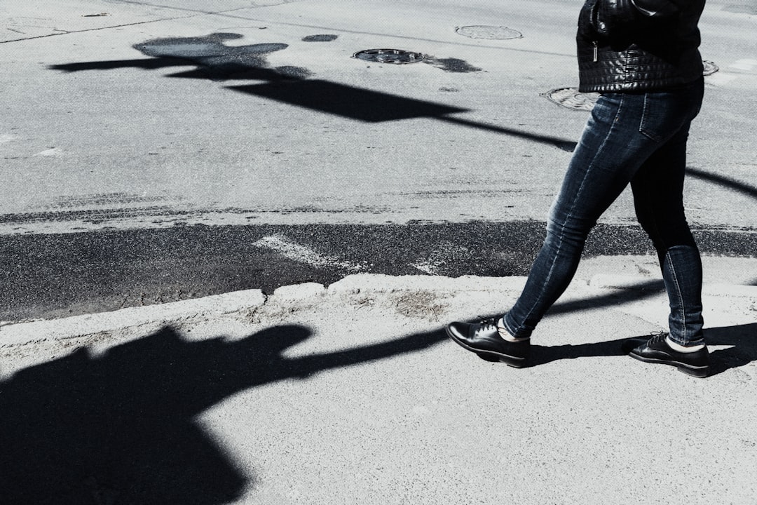 person in blue denim jeans and black shoes walking on gray concrete road during daytime