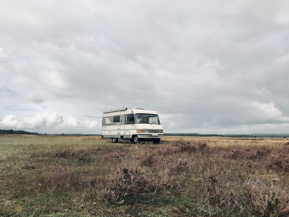 Weißer Lieferwagen tagsüber auf braunem Rasen unter weißen Wolken