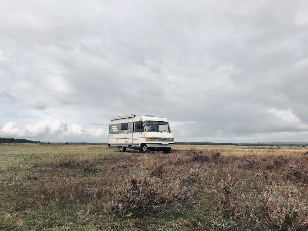 white van on brown grass field under white clouds during daytime