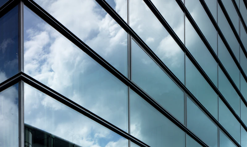 Klare Glasfront mit weißem Stahlrahmen und Himmelspiegelung