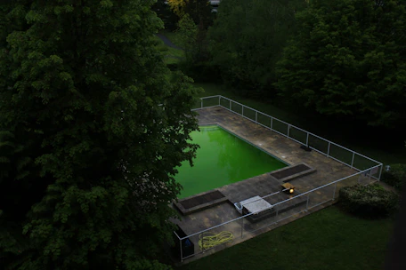 Sunlit private swimming pool surrounded by secure fencing and lush garden.