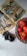 A vintage comic book is open on a white surface, showcasing colorful illustrations and speech bubbles. Next to the comic is an old-fashioned camera with a lens cap displaying text. A wicker basket filled with ripe red tomatoes sits nearby, adding a pop of color to the scene.