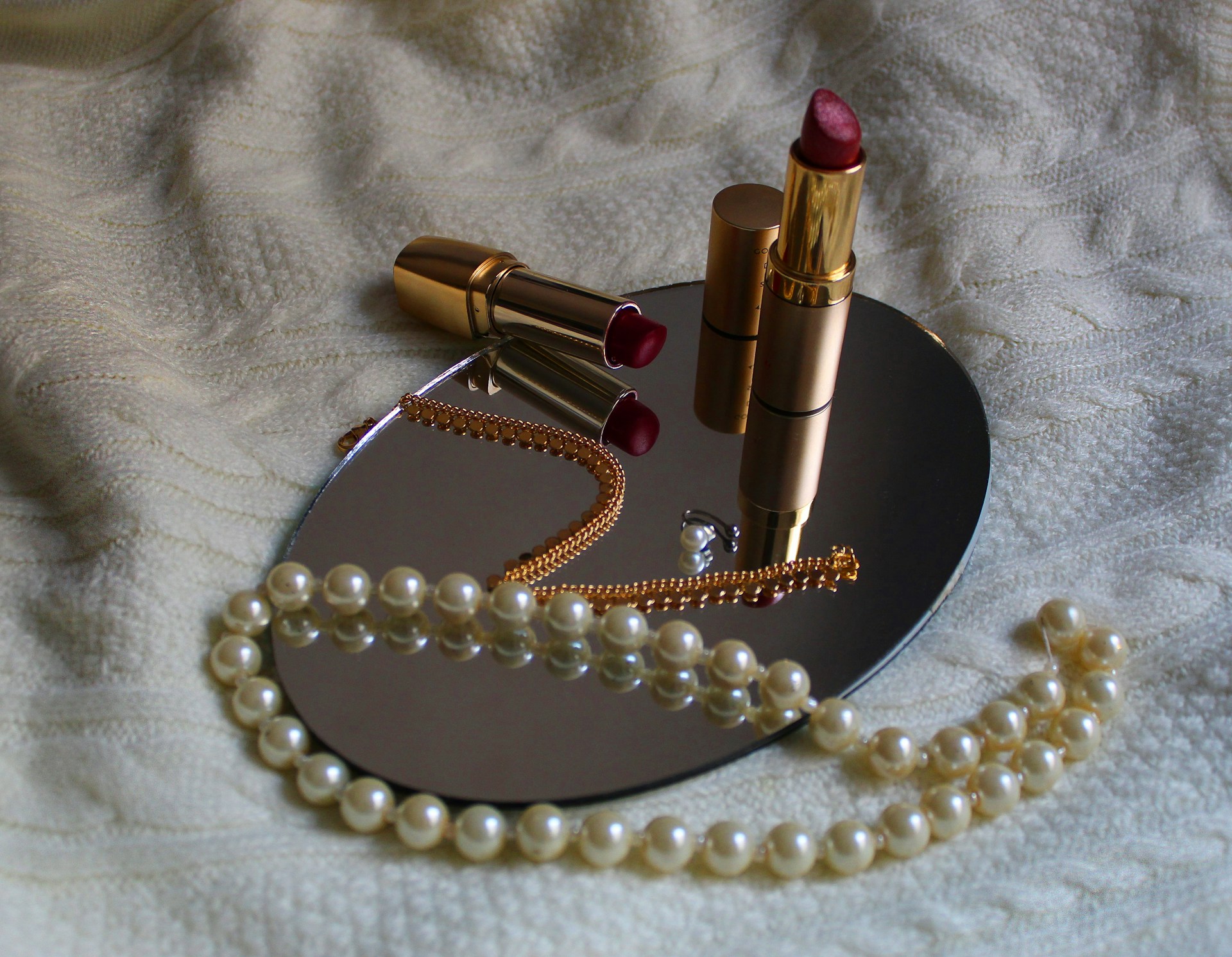 white pearl necklace beside pink lipstick