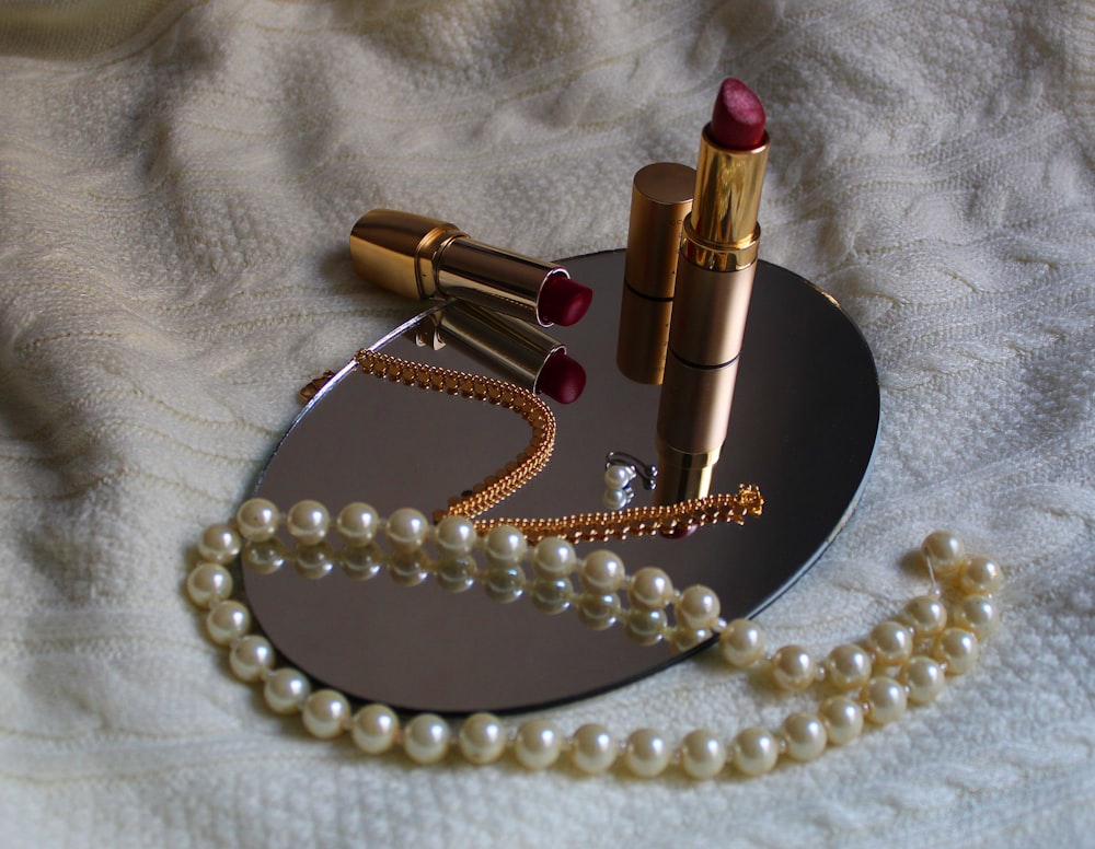 white pearl necklace beside pink lipstick