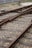 Railway tracks converge and diverge, surrounded by gravel and wooden sleepers. A metal signal or switch device is visible in the background, with a fence bordering the area.