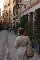 woman in white and black polka dot long sleeve shirt walking on sidewalk during daytime