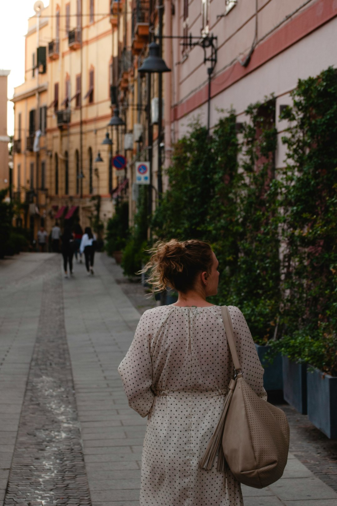 woman in white and black polka dot long sleeve shirt walking on sidewalk during daytime