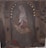 A painting depicts a seated woman adorned with a crown of stars, cradling a child in her arms. The background features architectural elements and muted, earthy tones. The woman is dressed in a robe with a veil, creating a serene, contemplative atmosphere.