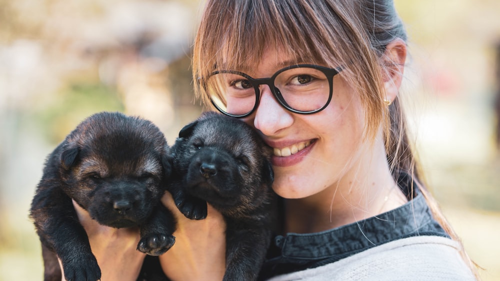 woman in black framed eyeglasses holding black short coated puppy