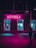 A neon-lit pharmacy with a vibrant pink sign illuminates the surrounding area. The windows display various items with a turquoise glow, contrasting with the pink light. A silhouette of a person is visible on the sidewalk, engrossed in their phone.