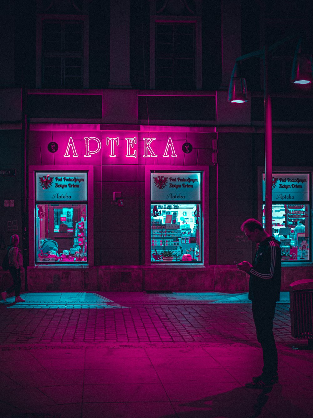 man in black jacket and pants standing near red and white store during night time