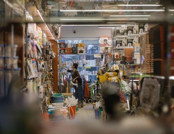 A busy hardware store aisle filled with tools and supplies, showing customers browsing.
