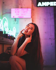 A close-up of a mischievous smile illuminated by neon lights during a private video chat.