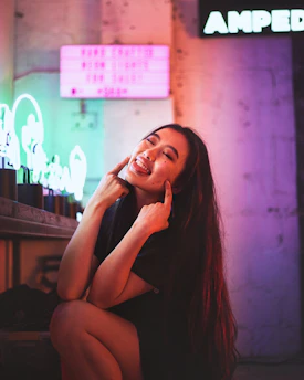 A close-up of a mischievous smile illuminated by neon lights during a private video chat.