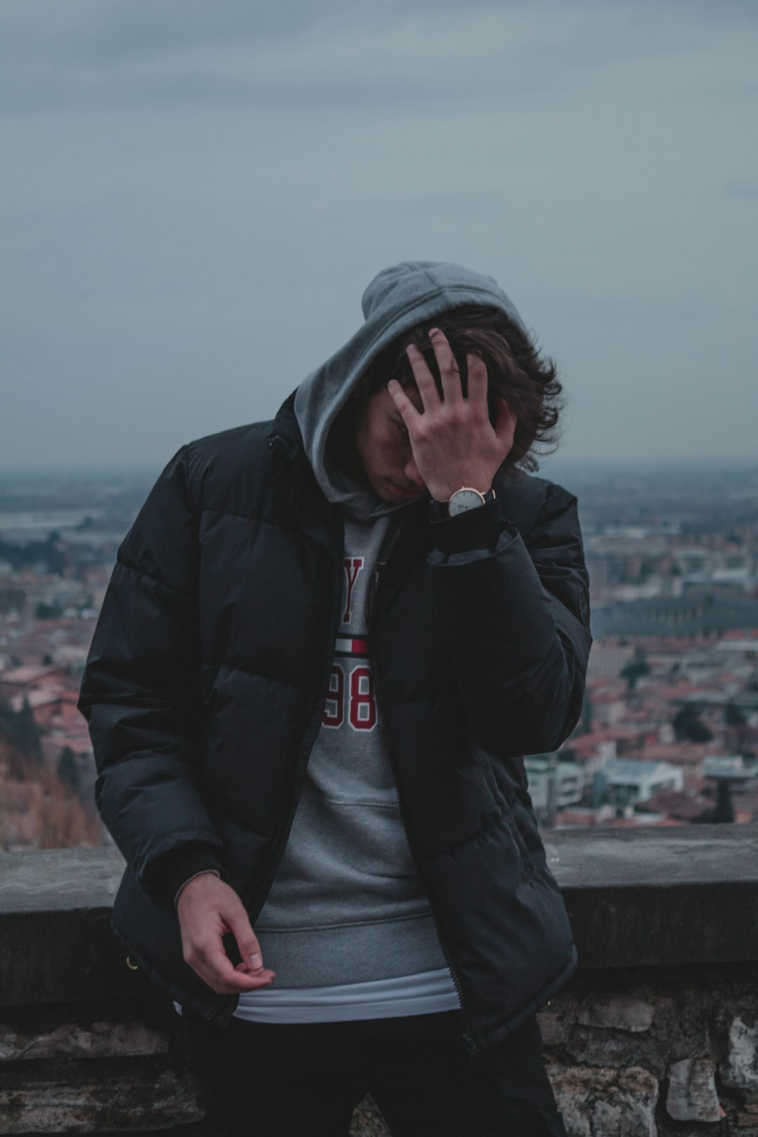 man in black zip up jacket and gray knit cap sitting on brown wooden fence during