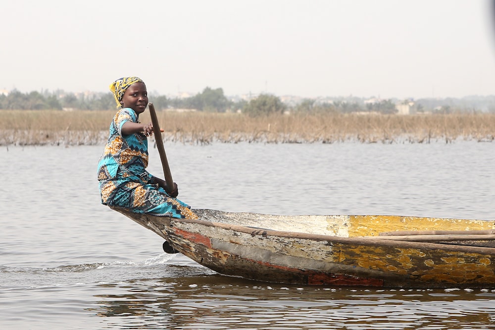 woman in blue and red dress riding on brown wooden boat on body of water during