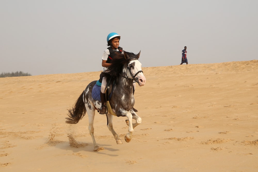 昼間の茶色の砂の上に黒と白の馬を着た男