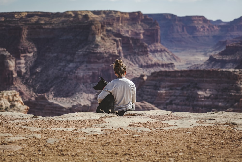 man in white shirt and black pants sitting on brown rock mountain during daytime