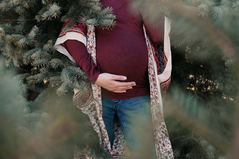 woman in red long sleeve shirt and blue denim jeans standing beside green christmas tree