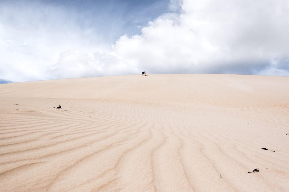 person walking on sand under blue sky during daytime