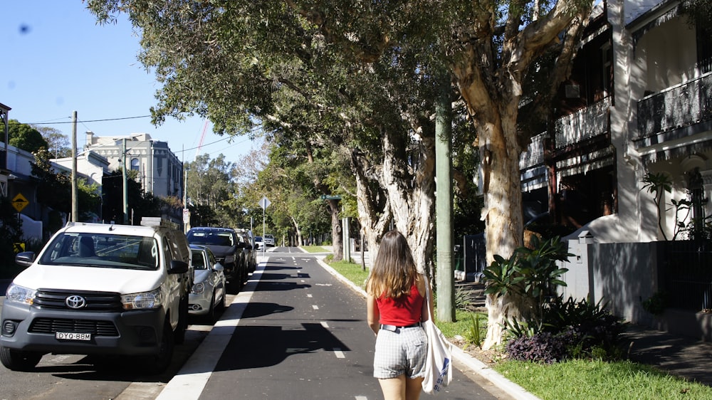 woman in red shirt and white pants walking on sidewalk during daytime