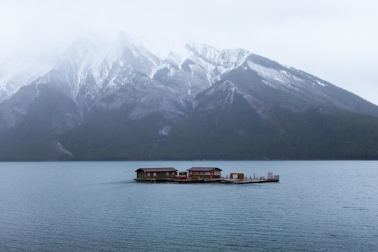 brown boat on sea near snow covered mountain during daytime in Lake Minnewanka Canada