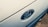 A close-up of a Ford car emblem displayed prominently on the vehicle's exterior. The oval-shaped emblem is surrounded by a chrome outline, set against the glossy surface of the car. The background has a smooth, metallic texture.