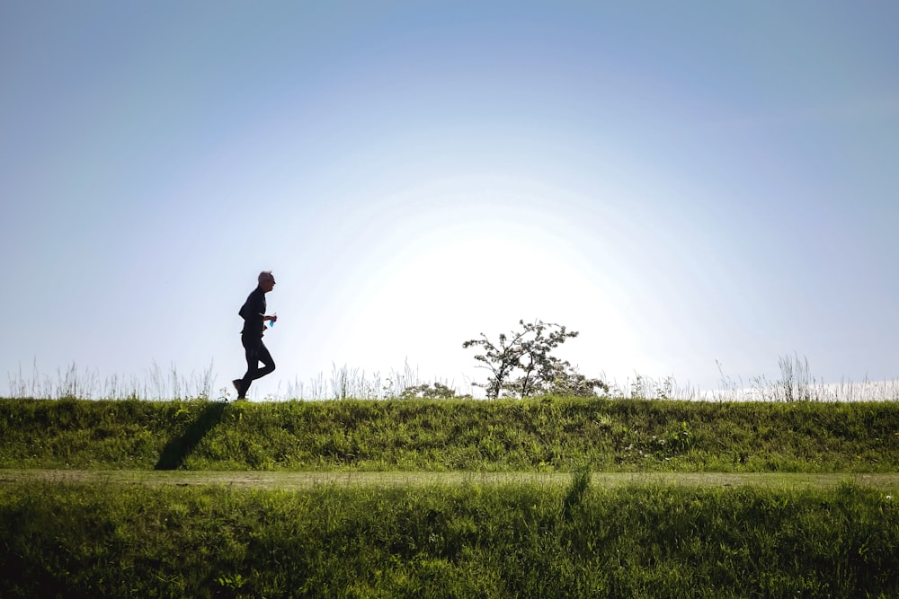 Hombre en chaqueta negra y pantalones corriendo en el campo de hierba verde durante el día