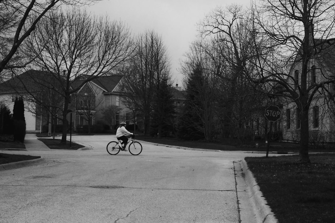 grayscale photo of man riding bicycle on road