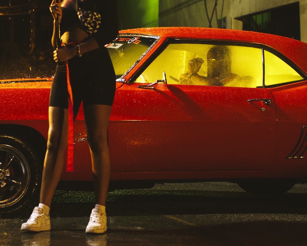 a woman standing in front of a red car