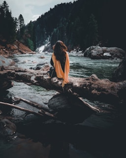 woman in orange dress standing on brown wooden log on river during daytime