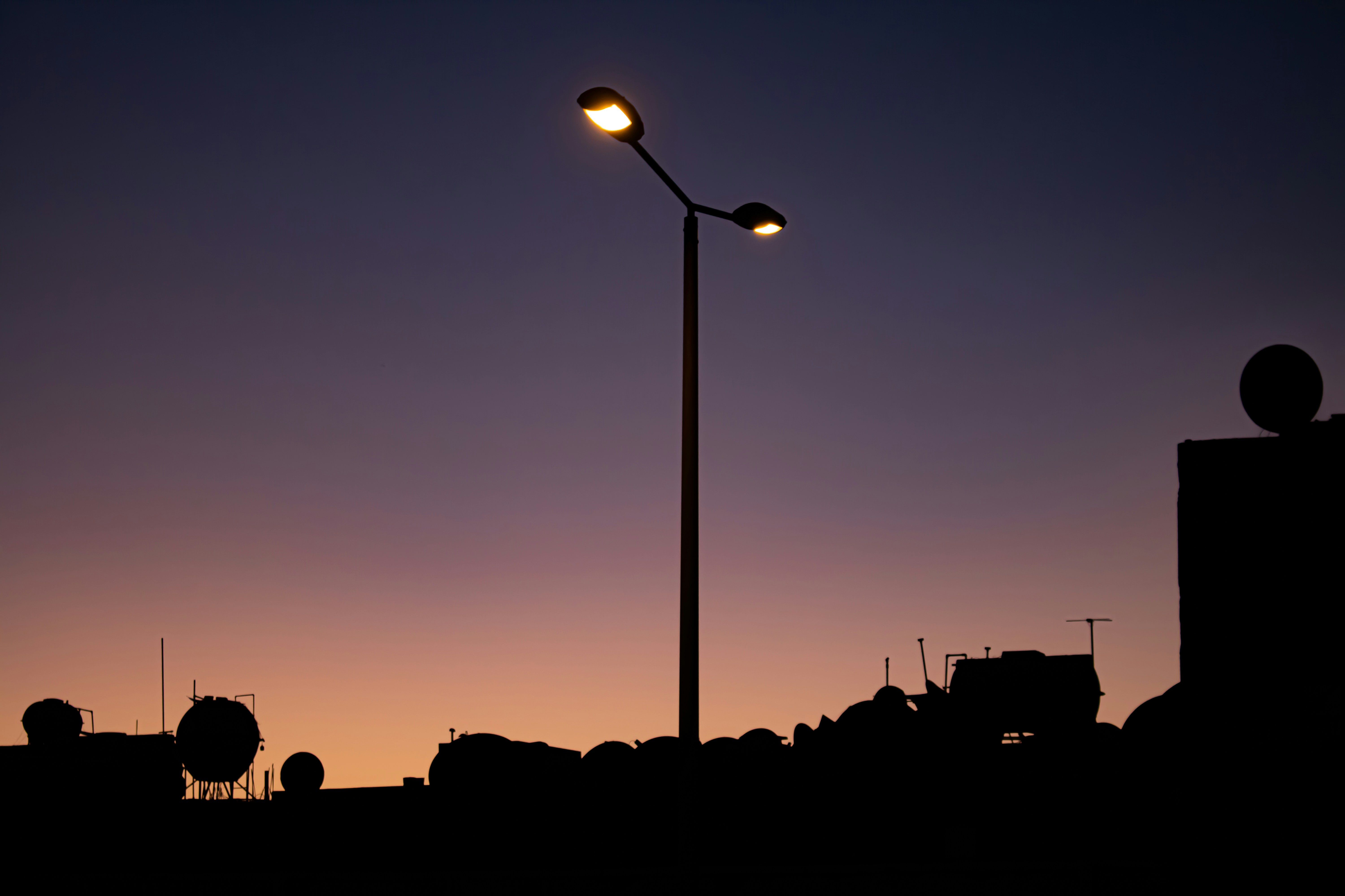 Oil storage tanks at dusk, dark industrial complex, silhouettes against dim sky, moody atmospheric lighting