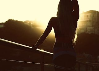 woman in white tank top and black shorts standing on balcony during sunset