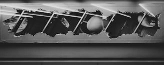 A rectangular frame with a ripped or torn effect revealing an underlying image of fragmented faces and objects, possibly glimpses of a person's face and other abstract shapes. The composition is monochromatic, predominantly in shades of black and white, with some diagonal lines crossing the image.