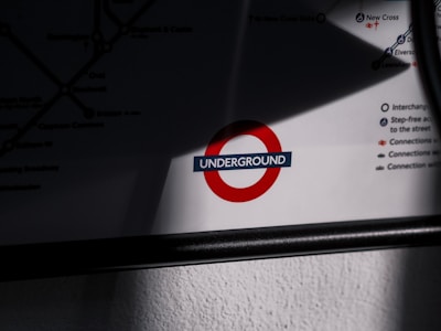 A segment of a map featuring a prominent red circle with a dark blue horizontal bar reading 'UNDERGROUND' in white letters. The map includes various lines and connections, partially visible, with an emphasis on interchange stations and accessibility options. Shadows and lighting create a contrast enhancing the map's logo.