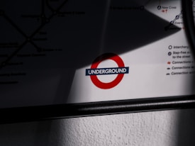 A segment of a map featuring a prominent red circle with a dark blue horizontal bar reading 'UNDERGROUND' in white letters. The map includes various lines and connections, partially visible, with an emphasis on interchange stations and accessibility options. Shadows and lighting create a contrast enhancing the map's logo.